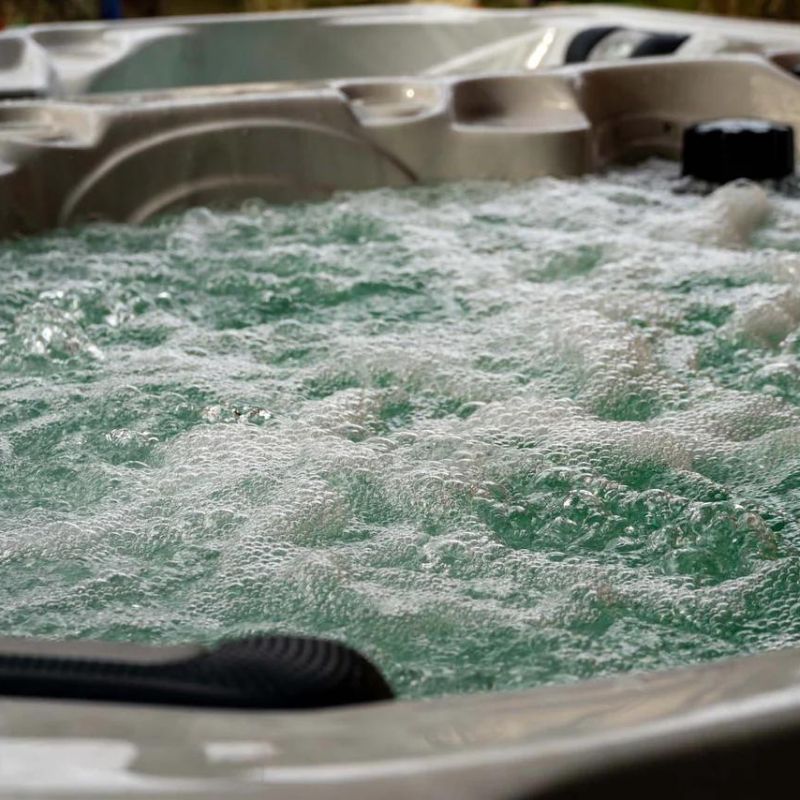 "Close-up of the Elevate Contrast Ice Bath with current by Passion Ice Baths and Wim Hof, showing bubbling water in the white interior. The bath features contoured seating and multiple jets in an outdoor setting."