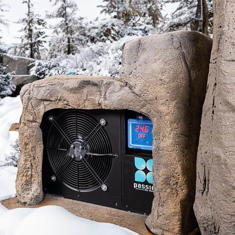 "Close-up of The Faith - Rock Ice Bath and Chiller by Passion Ice Baths and Wim Hof, highlighting the chiller unit integrated into the rock-textured design. The digital display shows the temperature, set in a snowy outdoor environment with trees in the background."