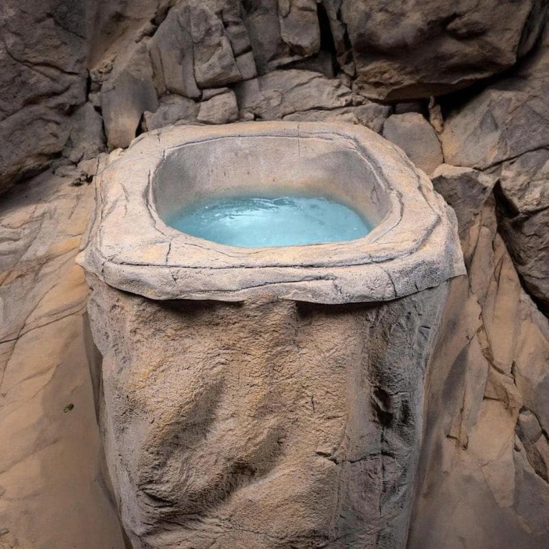 "The Faith - Rock Ice Bath and Chiller by Passion Ice Baths and Wim Hof, featuring a rock-textured design filled with water, set in a cave-like environment with natural rock formations surrounding the bath."