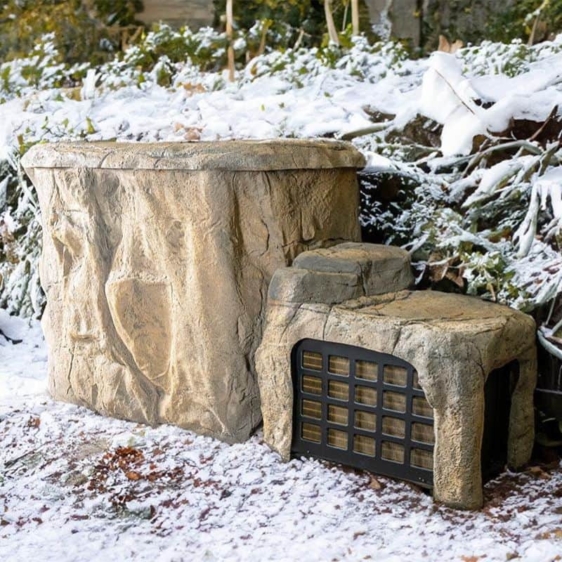 "The Faith - Rock Ice Bath and Chiller by Passion Ice Baths and Wim Hof, featuring a rock-textured ice bath and integrated chiller unit set outdoors in a snowy landscape. The design blends with natural surroundings, resembling a rock formation."