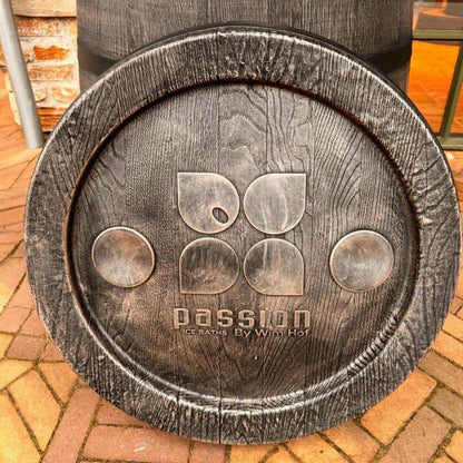 "Close-up of the lid of The Ice Man's Barrel by Passion Ice Baths and Wim Hof. The rustic wood-finished lid features the Passion Ice Baths logo and is set on a brick patio with part of the barrel visible in the background."