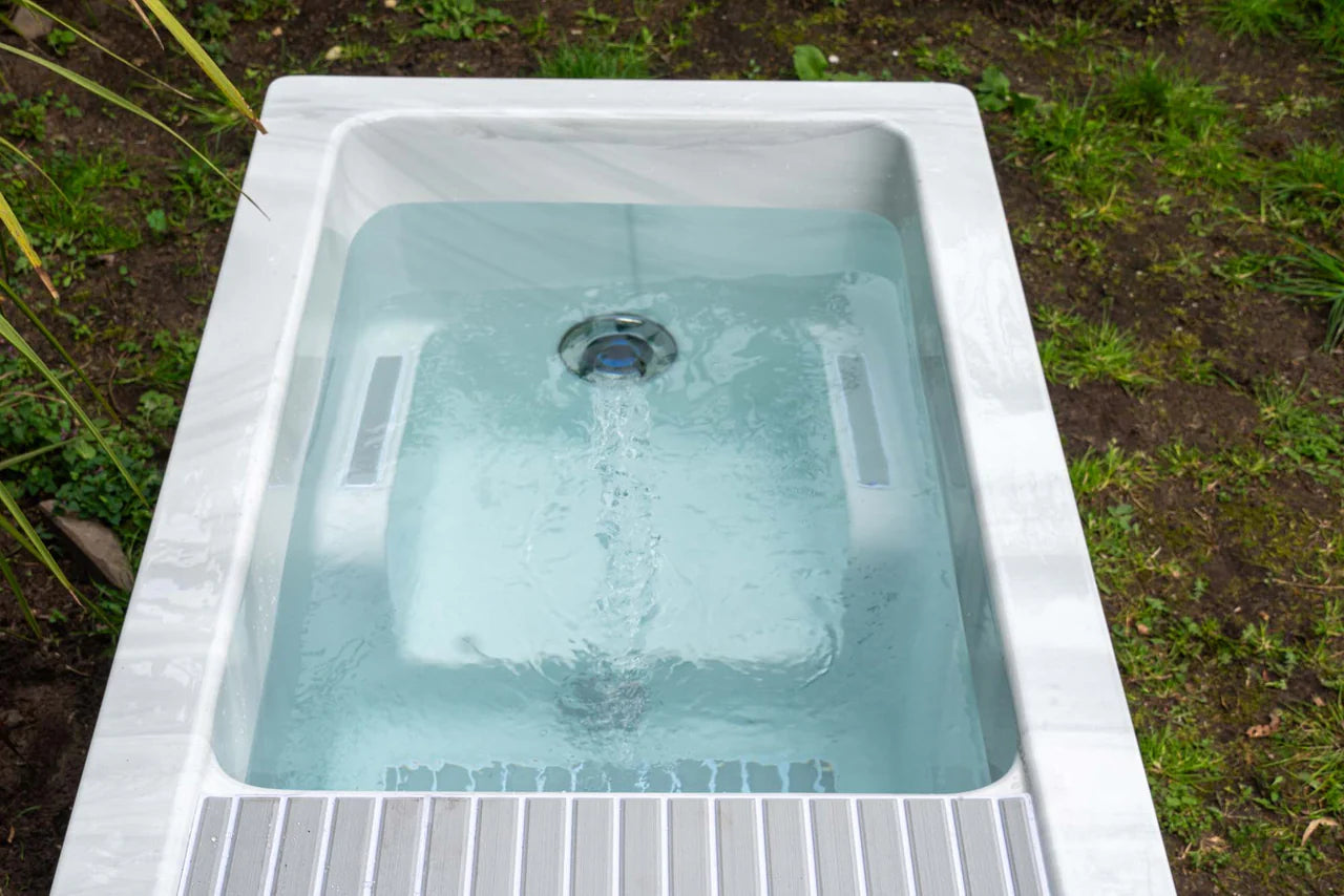 "Top view of the Breeze Ice Bath with current by Passion Ice Baths and Wim Hof, filled with water and showing the flow from the water jets. The white rectangular ice bath is set outdoors with greenery around."